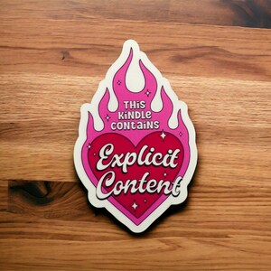 Op de afbeelding: Roze en witte sticker met een hartvorm en vlammen. Het hart zegt "Expliciete inhoud" en de vlammen zeggen "Deze Kindle bevat".