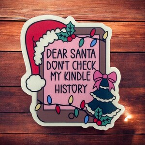 Puede incluir: Una pegatina rosa y blanca con un árbol de Navidad, un gorro de Papá Noel y el texto "Querido Papá Noel, no revises el historial de mi Kindle".