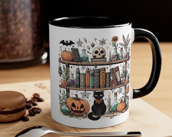 May include: White ceramic mug with a black interior and handle, featuring a Halloween-themed design. The design includes a bookshelf with pumpkins, a skull, potion bottles, a black cat, and books. A decorative and spooky mug.