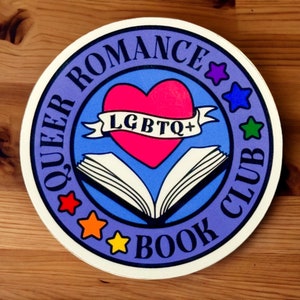 May include: A purple and blue round sticker with the text "Queer Romance Book Club" and a rainbow heart with the text "LGBTQ+" on a book.