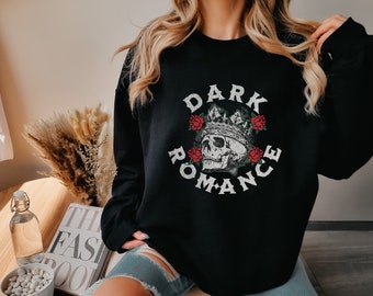 Peut inclure: Sweat-shirt noir avec un motif graphique représentant un crâne portant une couronne, entouré de roses rouges, et les mots "DARK ROMANCE" dans une police vieillie. Le motif est centré sur le devant du sweat-shirt.