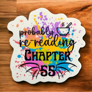 May include: A white sticker with a colorful splatter paint design. The sticker says "probably re-reading chapter 55" with a bowl and spoon graphic above the text.