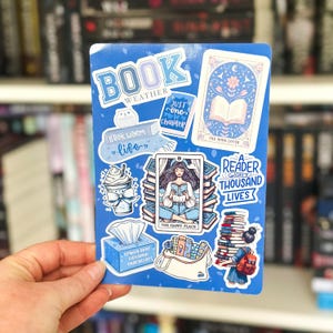 May include: A blue notebook adorned with book-themed stickers. The stickers feature phrases like "Book Weather" and "A Reader Lives a Thousand Lives". Other stickers show books, a tarot card, and a person reading, all on a blue background.