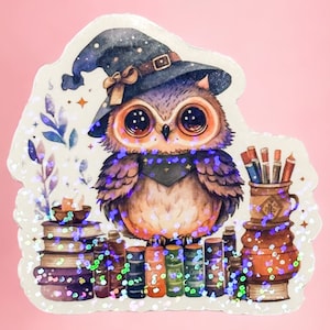 Op de afbeelding: Een fantasievolle uil met een heksenhoed zit op een stapel boeken met een pen en een inktpot ernaast. De uil heeft grote, ronde ogen en een bruin en paars gepatroneerd lichaam. De afbeelding heeft een glinsterende, iriserende achtergrond.