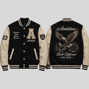 May include: A black and beige varsity jacket featuring a front letter A, the text Discipline Today Success Tomorrow, and the number 23. The back displays an eagle graphic above mountains and trees with the text Ambition Built Different EST. 2023.
