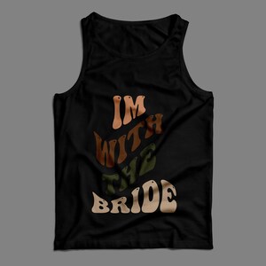 May include: Black tank top with the text "I'm with the bride" in a retro font with brown, orange, and green colors.