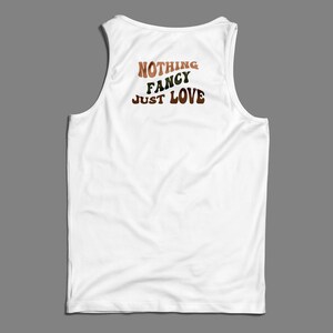 May include: White tank top with the text "NOTHING FANCY JUST LOVE" printed on the back in a retro font with brown, green, and orange colors.