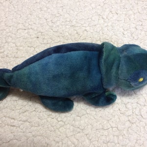 May include: A blue and green plush chameleon toy with a yellow eye. The toy is made of soft, fuzzy fabric and has a long tail.
