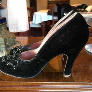 K&ouml;nnte beinhalten: Ein Paar schwarze Samt-High-Heel-Schuhe mit spitzer Zehenpartie und einem dekorativen Design aus silbernen Nieten. Die Schuhe haben ein rosafarbenes Futter und einen hohen Absatz.
