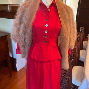 May include: A red dress with a matching jacket and a brown fur shawl. The dress has a fitted bodice and a full skirt. The jacket has a button-up front and a collar. The shawl is made of soft, fluffy fur.
