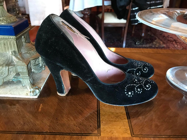 K&ouml;nnte beinhalten: Ein Paar schwarze Samt-High-Heels mit silbernen Verzierungen. Die Schuhe haben eine spitze Zehenpartie und einen geschlossenen R&uuml;cken.