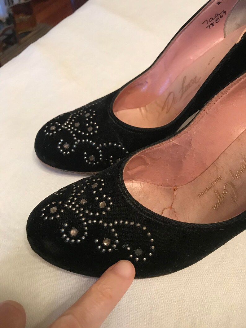 K&ouml;nnte beinhalten: Ein Paar schwarze Wildlederschuhe mit silbernen Nieten. Die Schuhe haben eine spitze Zehenpartie und einen niedrigen Absatz. Die Schuhe sind mit "De Luxe" gekennzeichnet und haben die Gr&ouml;&szlig;e "7 1/2 E 6 1/2" auf der Innenseite.