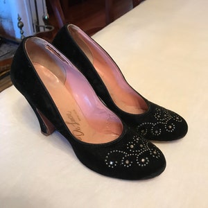 K&ouml;nnte beinhalten: Ein Paar schwarze Pumps aus Samt mit kleinem Absatz. Die Schuhe sind mit silberfarbenen Strasssteinen in einem Blumenmuster verziert. Die Schuhe sind auf der Innensohle mit "De Luchi" beschriftet.
