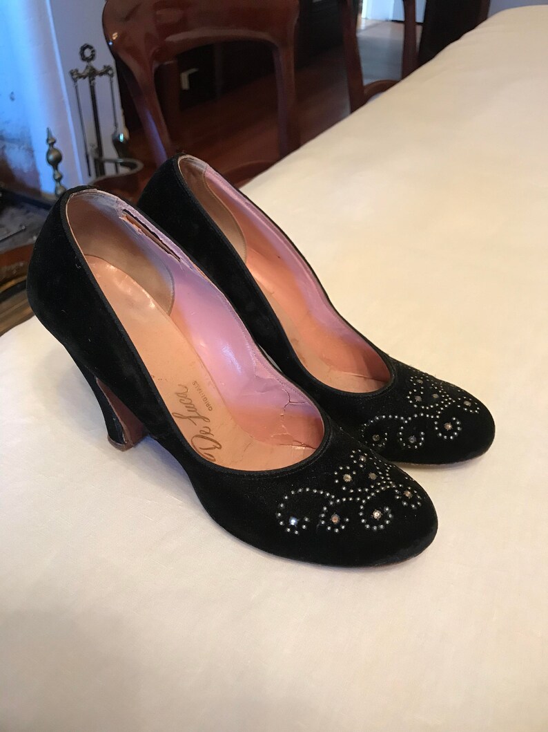 K&ouml;nnte beinhalten: Ein Paar schwarze Pumps aus Samt mit kleinem Absatz. Die Schuhe sind mit silberfarbenen Strasssteinen in einem Blumenmuster verziert. Die Schuhe sind auf der Innensohle mit "De Luchi" beschriftet.