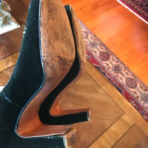 K&ouml;nnte beinhalten: Ein Paar schwarze Samt-Schuhe mit braunen Ledersohlen. Die Schuhe befinden sich auf einer Holzoberfl&auml;che.