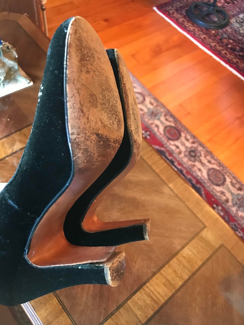 K&ouml;nnte beinhalten: Ein Paar schwarze Samt-Schuhe mit braunen Ledersohlen. Die Schuhe befinden sich auf einer Holzoberfl&auml;che.
