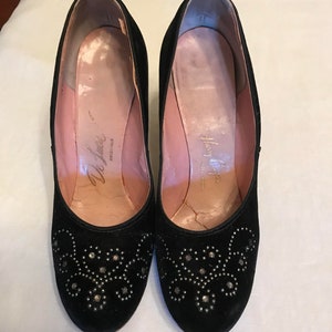 K&ouml;nnte beinhalten: Ein Paar schwarze Wildlederschuhe mit silbernen Nieten. Die Schuhe haben eine abgerundete Spitze und einen niedrigen Blockabsatz. Das Innere der Schuhe ist mit rosa Stoff gef&uuml;ttert und hat den Text "Delman Originals" auf der Innensohle.