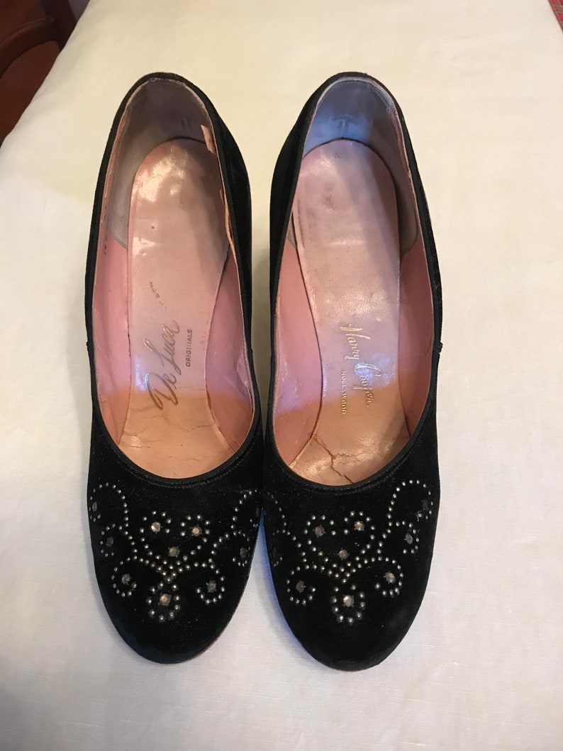 K&ouml;nnte beinhalten: Ein Paar schwarze Wildlederschuhe mit silbernen Nieten. Die Schuhe haben eine abgerundete Spitze und einen niedrigen Blockabsatz. Das Innere der Schuhe ist mit rosa Stoff gef&uuml;ttert und hat den Text "Delman Originals" auf der Innensohle.