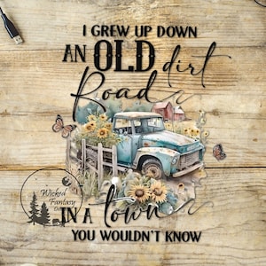 May include: A vintage blue pickup truck with a wooden fence and sunflowers in the bed. The truck is parked on a dirt road with a wooden sign that reads "I grew up down an old dirt road in a town you wouldn't know".