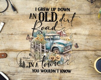 May include: A vintage blue pickup truck with a wooden fence and sunflowers in the bed. The truck is parked on a dirt road with a wooden sign that reads "I grew up down an old dirt road in a town you wouldn't know".