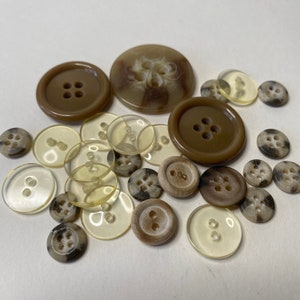 May include: A collection of brown and beige buttons in various shapes and sizes. Some buttons have a swirl pattern, while others have a simple design.