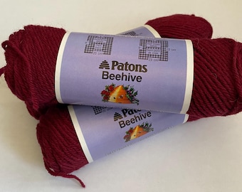 May include: Three skeins of Patons Beehive yarn in a deep burgundy red color. The yarn is labeled with the brand name and a grid showing stitch counts for different knitting and crochet techniques.