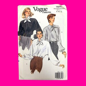 Puede incluir: Un sobre de patrón de costura Vogue Patterns, número 7840, para tallas 8-10-12. La ilustración muestra tres variantes de blusas: una camisa negra con lunares, una camisa blanca con lazo y una camisa a rayas con lazo, todas de manga larga.