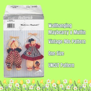 May include: Vintage 1990s sewing pattern for a wallhanging Maybearry & Muffin. The pattern is uncut and one size. The pattern envelope features a red and white checkered dress and blue and white checkered overalls.