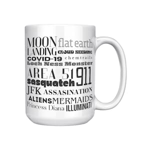 May include: White ceramic mug with a curved handle. The mug features black text including "MOON LANDING", "flat earth", "COVID-19", "Area 51", "Sasquatch", and other conspiracy-related terms.