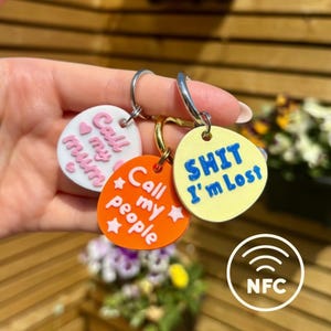 May include: Three novelty keyrings with amusing slogans. One is white with "Call my mum" in pink, another is orange with "Call my people" in white, and the third is yellow with "SHIT I'm Lost" in blue. Each keyring has a metal ring.