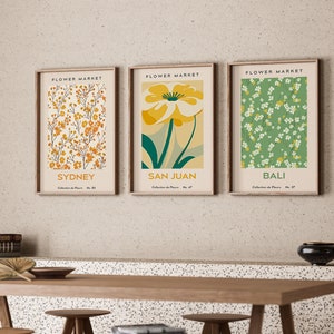 以下が含まれることがあります： 3つの額縁に入った花のプリント。各画像の上には「Flower Market」の文字が書かれている。プリントは、黄色、緑、白の花の模様が異なっている。各画像の下には「シドニー」、「サンフアン」、「バリ」の文字が書かれている。