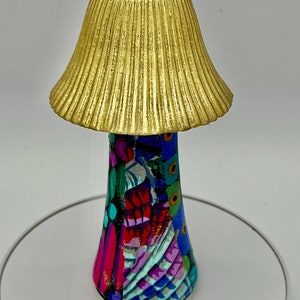 May include: A gold mushroom-shaped lamp with a colorful, patterned base. The lamp is sitting on a white surface.
