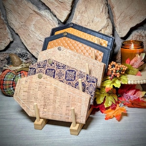 May include: A display of coffin-shaped wallets in various materials and patterns. The wallets are displayed on a wooden stand. The patterns include cork, embossed orange leather, and a blue and white tile design. The background includes fall-themed decorations.