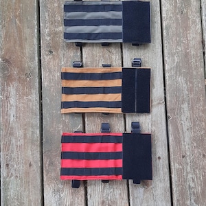 May include: Three tactical pouches with black hook and loop closures. The pouches are made of fabric with black and gray stripes, black and brown stripes, and black and red stripes.