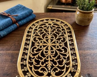 Salvamanteles ovalado de hierro fundido ornamentado con diseño de volutas.
