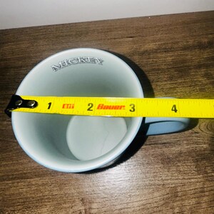 Peut inclure: Une tasse en c&eacute;ramique bleu clair avec le mot "MICKEY" imprim&eacute; sur le bord. La tasse a une anse bleu clair et mesure environ 7,6 cm de diam&egrave;tre.