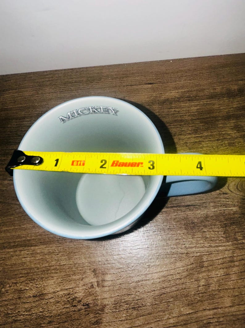 Peut inclure: Une tasse en c&eacute;ramique bleu clair avec le mot "MICKEY" imprim&eacute; sur le bord. La tasse a une anse bleu clair et mesure environ 7,6 cm de diam&egrave;tre.