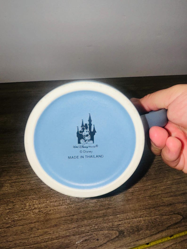 Peut inclure: Une tasse en c&eacute;ramique bleue et blanche avec un int&eacute;rieur bleu clair. Le fond de la tasse pr&eacute;sente un motif de ch&acirc;teau avec Mickey Mouse, le texte "Walt Disney World", "&copy; Disney" et "MADE IN THAILAND".