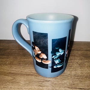 Peut inclure: Une tasse en c&eacute;ramique bleu clair avec Mickey Mouse dans deux poses diff&eacute;rentes. La tasse a une anse incurv&eacute;e et un int&eacute;rieur bleu clair. Les images de Mickey sont sur un fond bleu fonc&eacute;.