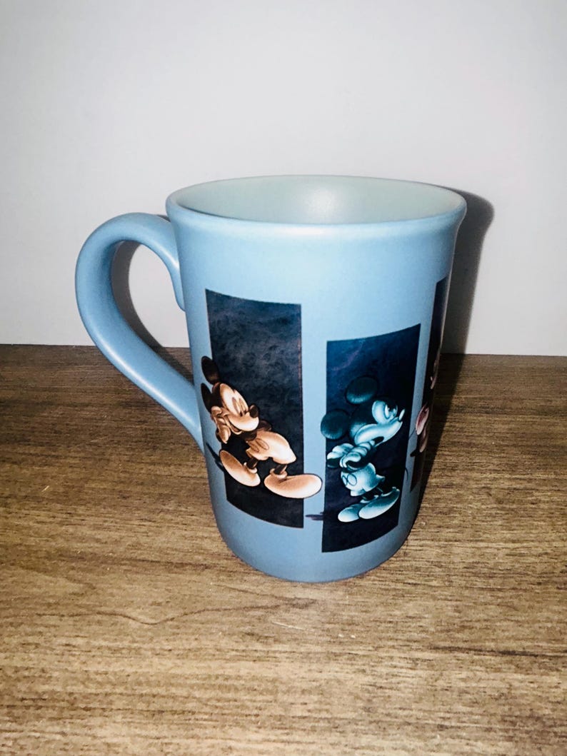 Peut inclure: Une tasse en c&eacute;ramique bleu clair avec Mickey Mouse dans deux poses diff&eacute;rentes. La tasse a une anse incurv&eacute;e et un int&eacute;rieur bleu clair. Les images de Mickey sont sur un fond bleu fonc&eacute;.