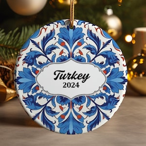 May include: A round ceramic Christmas ornament with a blue and white floral pattern. The ornament has a white label with the text "Turkey 2024".