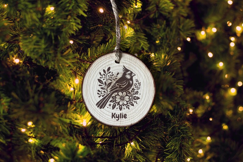 Handmade rustic sliced wood ornament featuring a floral bird design, with delicate flowers and leaves surrounding the bird. The ornament is custom personalized with a name, and the design is laser engraved for a unique, thoughtful home décor gift.
