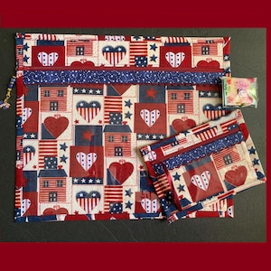 Pode incluir: Um conjunto de duas bolsas com z&iacute;per de tem&aacute;tica patri&oacute;tica. A bolsa maior apresenta um padr&atilde;o repetido de cora&ccedil;&otilde;es, casas e bandeiras americanas em vermelho, branco e azul. A bolsa menor espelha o design. Ambas t&ecirc;m z&iacute;peres e acabamentos azuis.