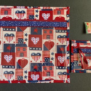 Pode incluir: Um conjunto de bolsas de tecido com tema patri&oacute;tico e um pequeno pacote. As bolsas apresentam um padr&atilde;o repetido de cora&ccedil;&otilde;es, casas e estrelas em vermelho, branco e azul. Uma bolsa tem um z&iacute;per e um berloque de contas.