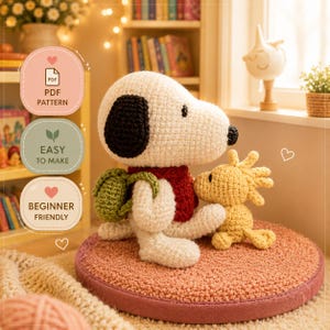 May include: A crocheted Snoopy doll with a black ear, a red scarf, and a green backpack sits beside a yellow Woodstock doll. The dolls are on a pink cushion. The image includes text that says "PDF Pattern", "Easy to Make", and "Beginner Friendly".