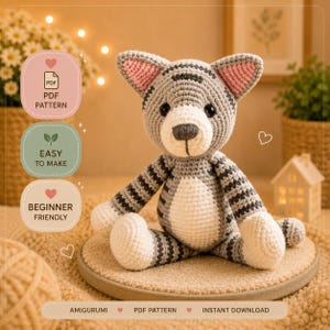 Könnte beinhalten: Ein handgehäkeltes Katzen-Amigurumi in Grau und Weiß, mit schwarzen Streifen und rosa Ohren. Das Stofftier sitzt auf einer runden, hellbraunen Oberfläche. Der Text auf dem Bild lautet "PDF Pattern", "Easy to Make" und "Beginner Friendly".