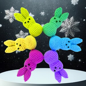 May include: Six crocheted Easter bunny plushies in a circle. The bunnies are yellow, green, blue, purple, pink, and light green. They are all facing inward towards the center of the circle.