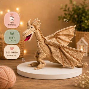 Puede incluir: Un dragón tejido a ganchillo en hilo color beige, con alas detalladas y una lengua roja. El dragón está posado sobre una plataforma blanca. La imagen incluye texto que dice "PDF Pattern", "Easy to Make" y "Beginner Friendly".