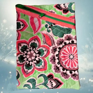 Könnte beinhalten: Eine grüne, rosa und schwarze gesteppte Reißverschlusstasche mit einem Blumenmuster. Die Tasche hat einen Reißverschluss und einen rosa Reißverschluss-Zipper.