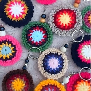 Puede incluir: Una colección de llaveros de ganchillo coloridos con diferentes patrones y diseños. Cada llavero presenta una pieza circular de ganchillo con un diseño central y un anillo de metal para sujetar las llaves.